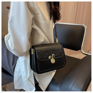Detail of black crossbody bag with embossed patterns and gold bunny-shaped clasp