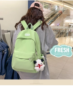 Detail of light green waterproof backpack featuring a cute white puppy plush keychain
