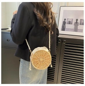 Detail of round straw bag featuring pearl strap and drawstring lining on model
