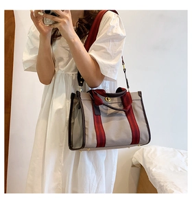 Detail of grey canvas tote with leather trim and striped shoulder strap in use