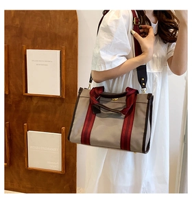 Taupe canvas tote bag with brown leather trim and red striped webbing worn crossbody