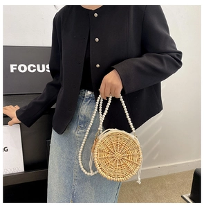 Detail of round straw woven bag featuring a white pearl strap and drawstring lining