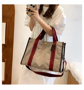 Detail of canvas tote bag featuring burgundy striped straps and golden turn-lock closure
