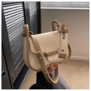 Detail of a beige leather crossbody bag with brown trim and gold metal logo hardware
