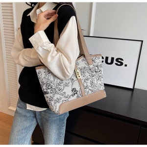 Detail of canvas tote bag with floral patterns, brown leather trim, and metal twist lock