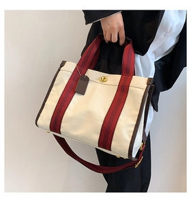 Detail of off-white canvas tote with reddish-brown striped handles and gold twist-lock