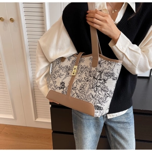 Detail of canvas tote bag with black floral print and brown leather trim on a model