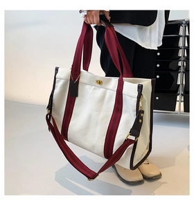 Close-up of canvas tote bag featuring striped handles and golden turn-lock closure