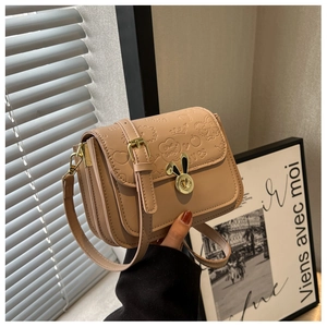 Macro detail of a beige crossbody bag featuring a golden bunny-shaped twist lock