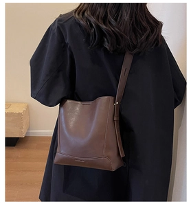 Vista dettagliata della borsa a secchiello marrone indossata con un cappotto nero
