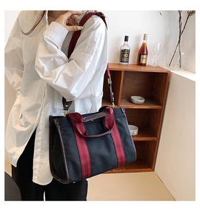 Detail of black canvas tote bag with red striped handles and brown leather trim accents