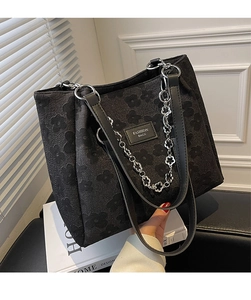 Détail d'un sac cabas noir à fleurs gaufrées avec chaîne argentée et bandoulière en cuir