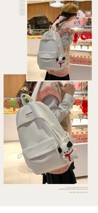 Detail showing white canvas backpack with brand label and plush puppy keychain accessory
