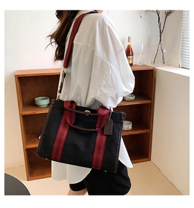 Detail of canvas tote bag with red-brown striped webbing and premium leather trim