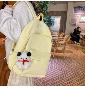 Detail of light yellow nylon backpack with a cute white dog plush pendant in a cafe setting