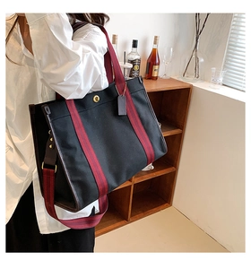 Black canvas tote bag with red striped straps and gold clasp shown on a model