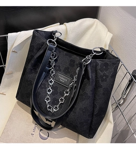 Détail de la texture florale gaufrée et chaîne argentée sur le sac cabas noir