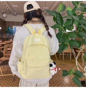 Detail view of light yellow canvas backpack with cute puppy plush charm in a cafe