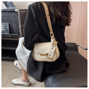 Detail view of cream and brown crossbody bag with fashion canvas strap and metal logo