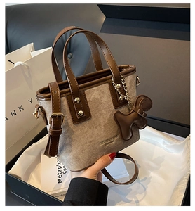 Detail of suede bucket bag with brown leather trim, bear charm and brand gift packaging