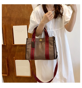 Detail of dark brown tote bag featuring red and black striped straps and metal turn-lock