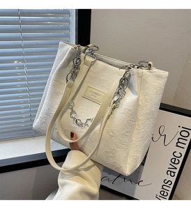 Gros plan du sac cabas blanc crème avec gaufrage floral et breloque chaîne fleurie