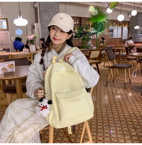 Pale yellow nylon backpack with cute puppy pendant shown in a cozy cafe setting