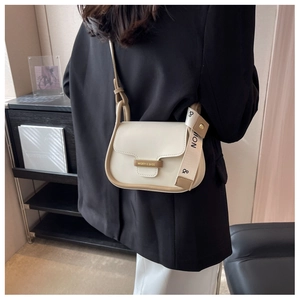 Detail of minimalist beige crossbody bag with MQIER metallic nameplate on mannequin