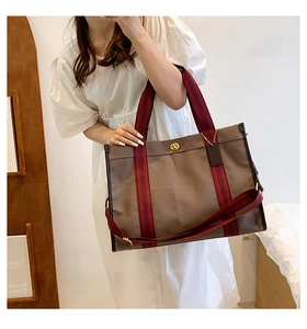 Detail view of a large brown tote bag showing the metal twist-lock and striped strap handles