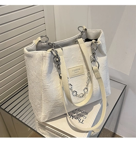 Détail du sac cabas jacquard blanc avec texture florale, chaîne argentée et poignée en cuir