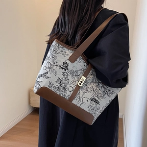 Large floral canvas tote bag with brown faux leather trim shown on shoulder of a model