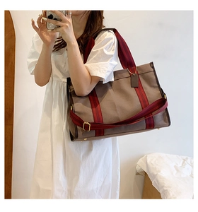 Detail of canvas tote bag featuring red and black striped handles and side metal buckle