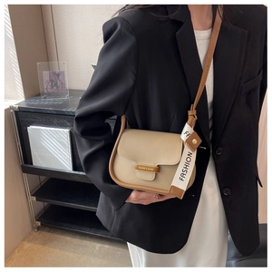 Detail of beige flap crossbody bag with brown trim and fashion letter ribbon decoration