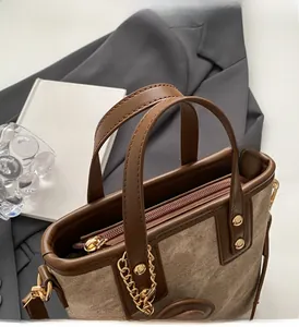 Detail of a brown canvas handbag with leather handles and premium metal chain accents