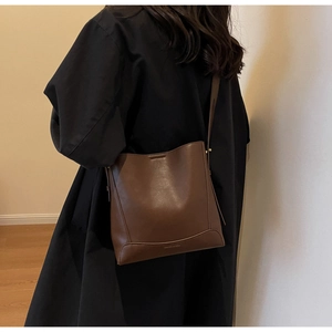 Dettaglio della borsa a secchiello in pelle marrone scuro su modella con texture vintage