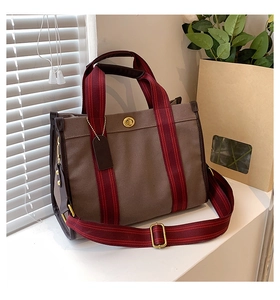 Close-up of brown canvas tote with signature red and black striped straps and turn-lock