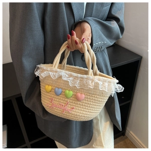 Detail of hand-woven straw bag with lace trim, colorful heart charms and embroidery