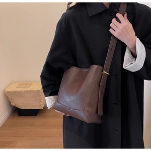Dettaglio di una borsa a secchiello in pelle opaca marrone scuro con tracolla larga regolabile