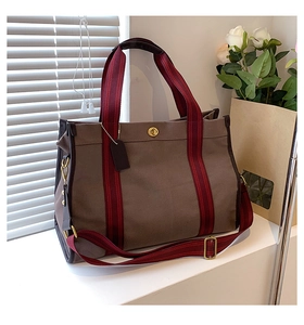 Detail of canvas tote bag with red-black striped handles and golden turn-lock closure