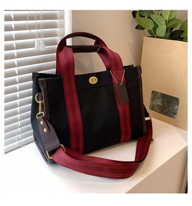 Detailed shot of black canvas tote bag with burgundy webbing and golden turnlock closure