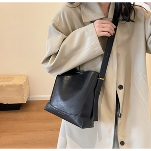 Dettaglio borsa a secchiello nera con texture in pelle sintetica e fibbia dorata elegante