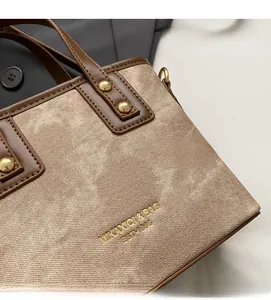 Macro detail of tote bag showing light coffee fabric texture and leather piping with studs