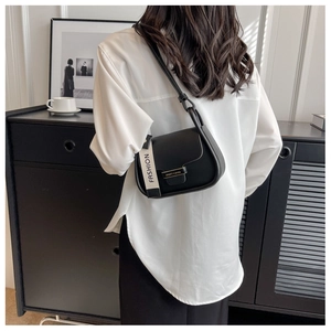 Detailed back view of a black semi-round flap bag with wide fashion strap on model