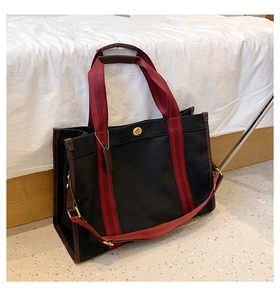 Detail of black canvas tote bag with red and black striped handles and golden turn lock
