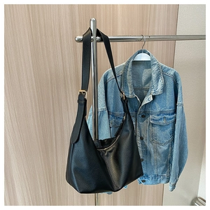 Detail of black hobo bag with pebble leather texture and gold hardware hanging on a rack