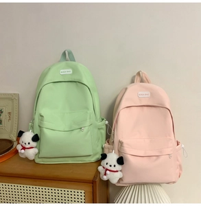 Detail of light green and pink canvas backpacks with cute plush puppy charms on a cabinet