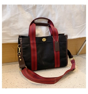 Detail of canvas tote bag with red striped handles, leather trim, and gold twist lock