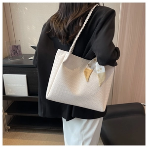 Detail of off-white houndstooth tote bag with woven strap and silk scarf worn by model