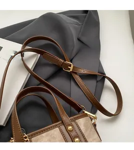 Detail of a brown leather and canvas bucket bag with gold buckles on a suit jacket