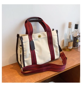 Detail view of canvas tote with leather trim, red-black webbing and golden turn-lock